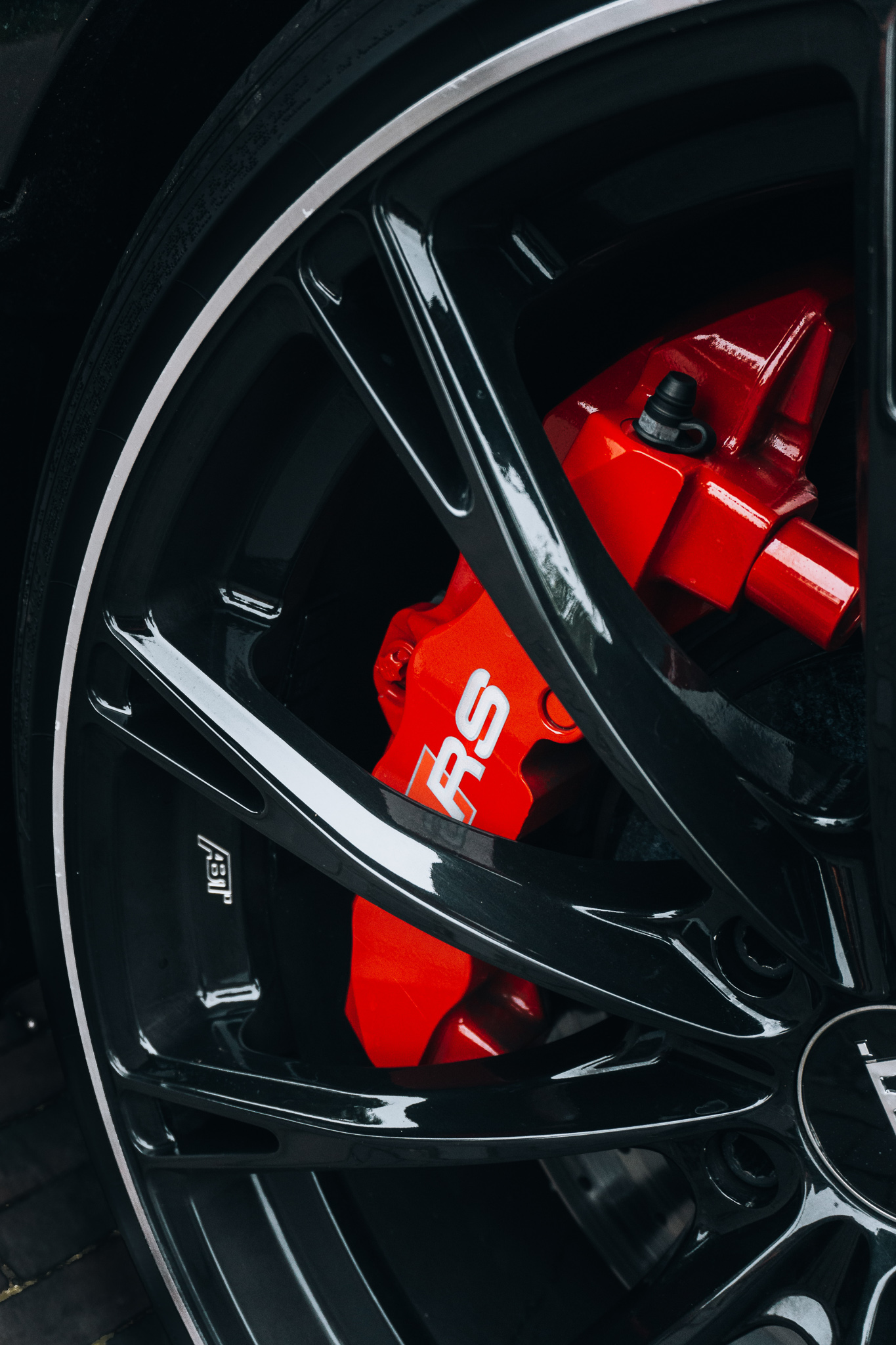 This image shows a caliper painted red tucked behind the black spokes of a designer performance racing wheel.